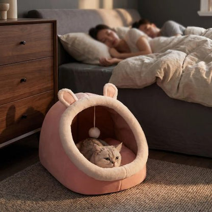 Un chat se repose paisiblement dans la niche Confort PLAYZONE™, placée près du lit, pendant que ses humains dorment.