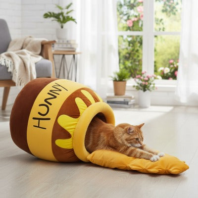 Chat étiré sur le coussin du panier Pot de Miel posé au sol près d’une fenêtre, profitant d’un espace lumineux et confortable